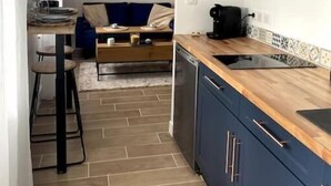 Cocina compacta con armarios azul oscuro, encimera de madera y comedor con sofá azul y una máquina de café.