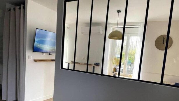 Un dormitorio con cama, televisor montado en la pared, ventana con vistas y espejo con barras verticales.