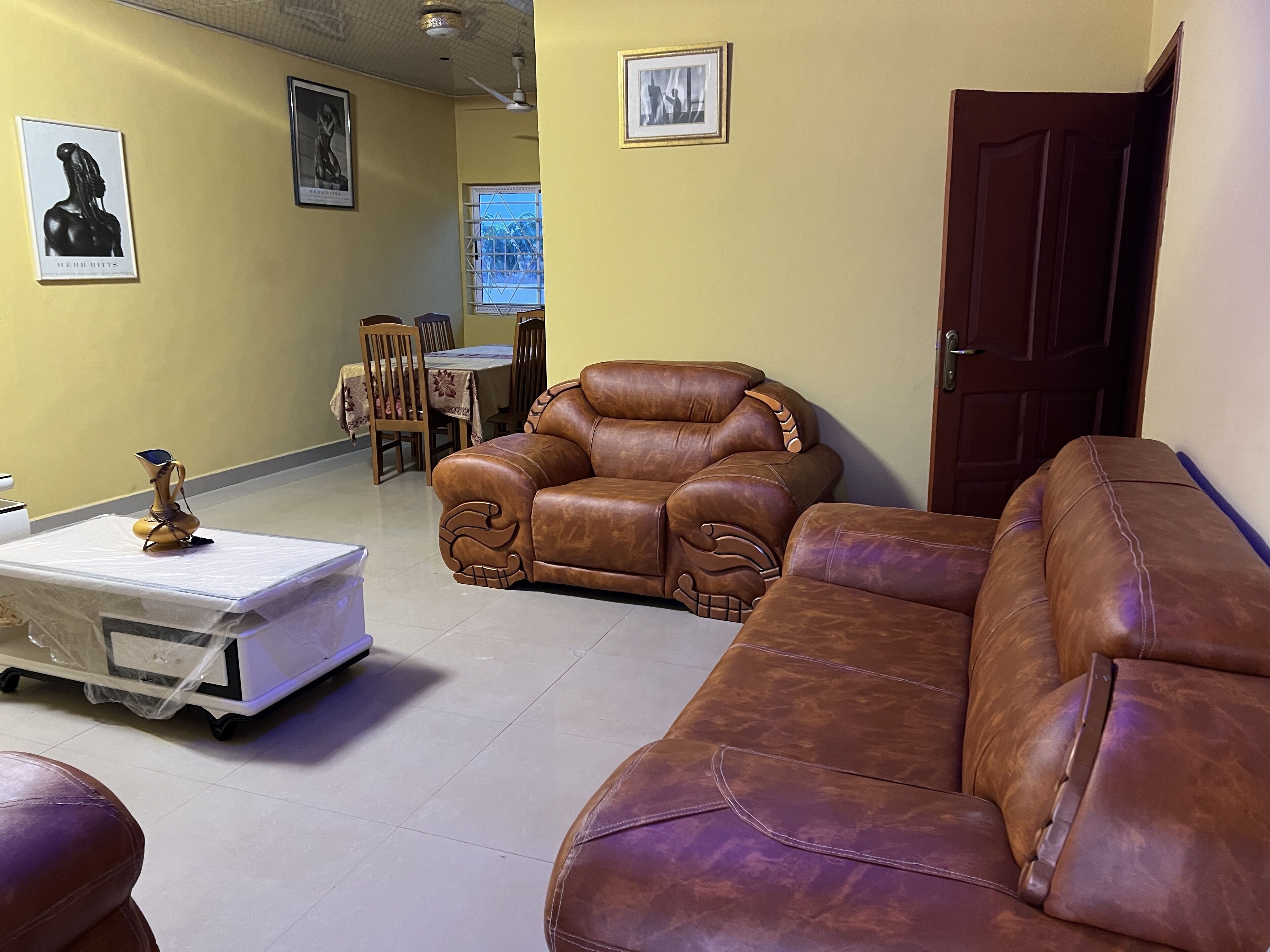 Un salon avec un canapé en cuir marron, une table basse et un coin repas comprenant des chaises et une table.
