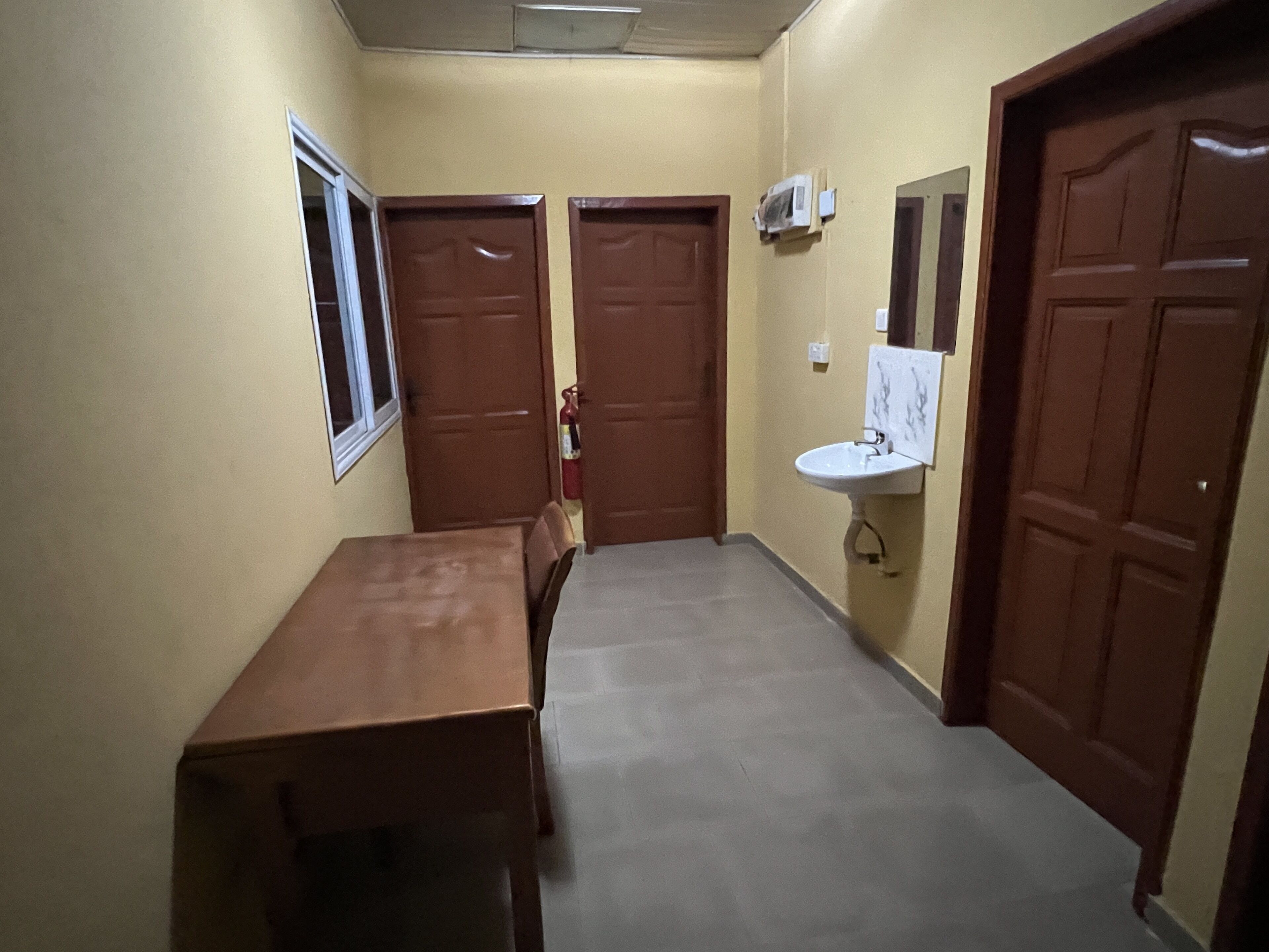 A narrow hallway with a wooden table and chairs, a white sink, and two wooden doors.