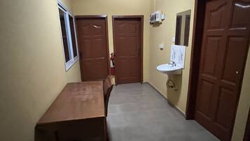 A narrow hallway with a wooden table and chairs, a white sink, and two wooden doors.