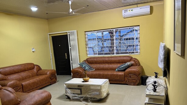 A living room with two brown leather sofas, a coffee table, a TV, and a window with metal bars. - Naayina Vacation Villas (Kogni)