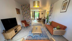A living room with a flat-screen TV, orange sofa, and wicker chairs. - Appartement Avec Jardin en Plein Cœur de Barbizon (Barbizon)