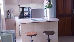 A modern kitchen with wooden cabinets, a central island with stools, pendant lighting, and a refrigerator.