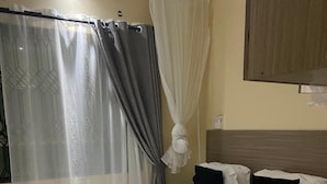 A hotel room with a bed, a bedside table, a curtain, and a headboard.