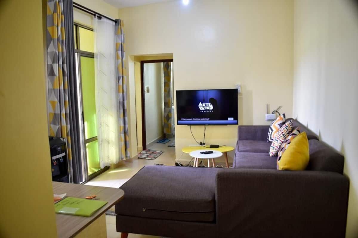 A living room with a sofa, a small table, and a TV on the wall.