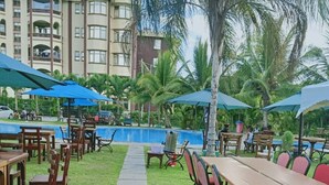 An outdoor dining area with tables and chairs, a pool, and palm trees.
