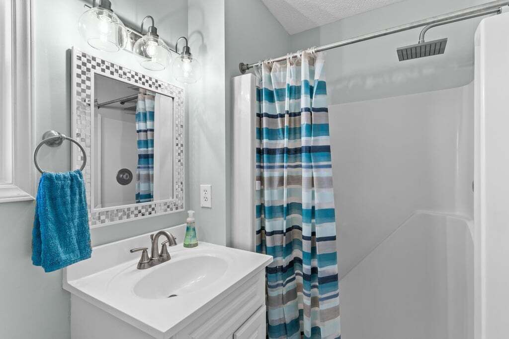 A bathroom with a white sink, a mirror with a decorative frame, a towel ring with a blue towel, and a shower with a striped curtain.
