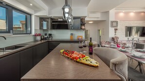 A modern kitchen with a central island, a dining area with a chandelier, and a view of the outside. - Villa Lorena Dalmacija (Nin)