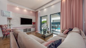 A modern living room with a sofa, a glass coffee table, a flat-screen TV, and a fireplace. - Villa Lorena Dalmacija (Nin)