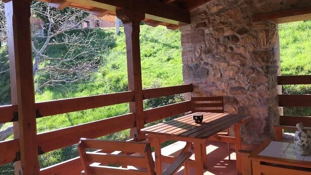 A wooden deck with a stone wall, wooden benches, and a table with a cup and saucer. - Vivienda Vacacional Naguar Para 4 Personas en Triongo, Cangas de Onís (Triongo, Cangas de Onís)