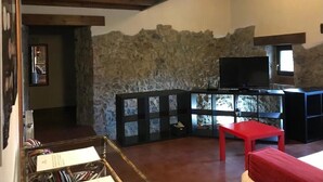 A cozy living room with a stone wall, a television, and a red table. - Vivienda Vacacional Naguar Para 4 Personas en Triongo, Cangas de Onís (Triongo, Cangas de Onís)