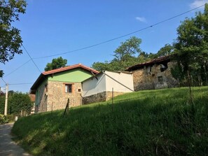 Un paysage rural avec une maison en pierre et un bâtiment surmonté d’un toit végétalisé, le tout entouré de verdure et sous un ciel dégagé.
