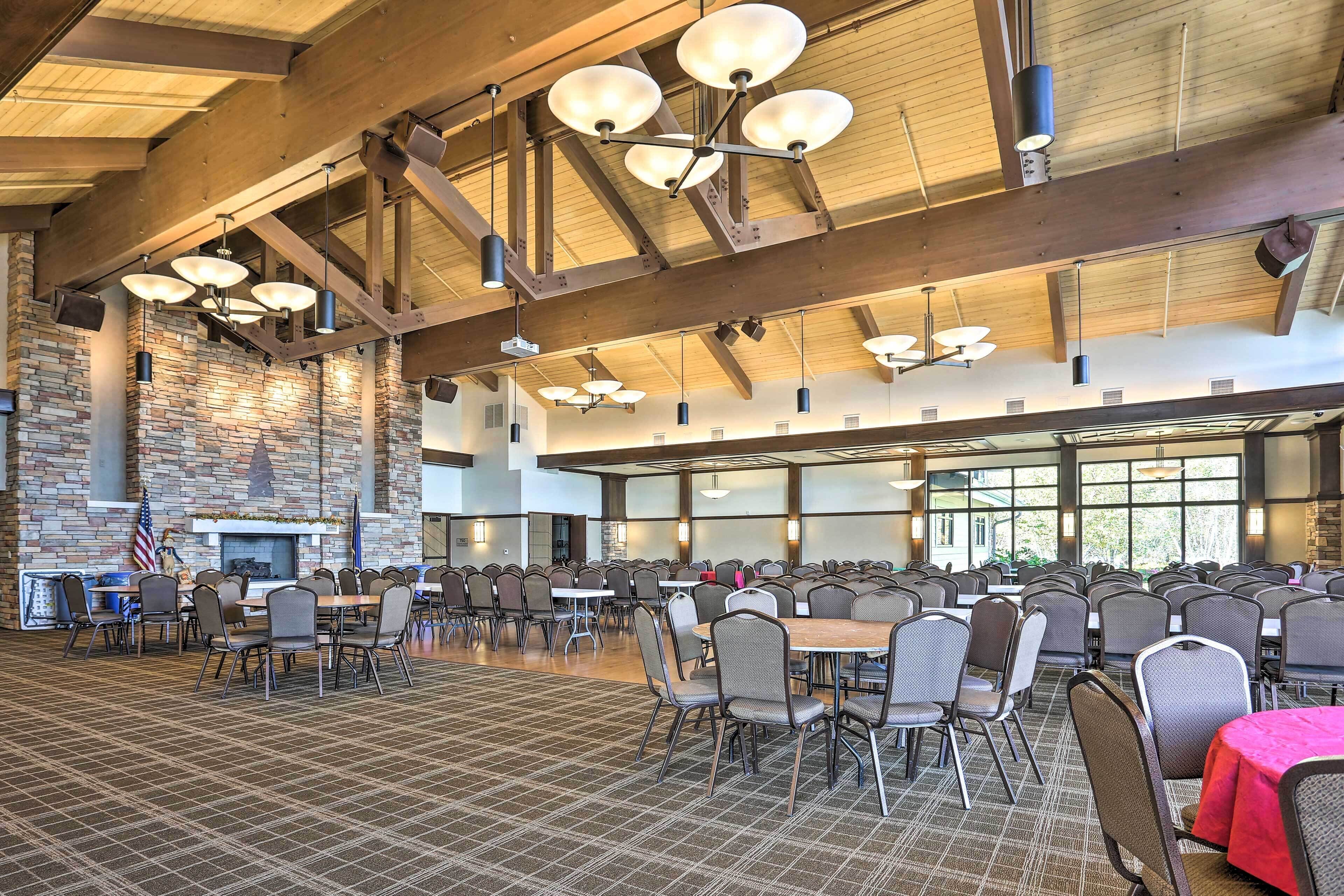 A spacious indoor dining area with multiple tables and chairs, a brick wall, and large windows allowing natural light.