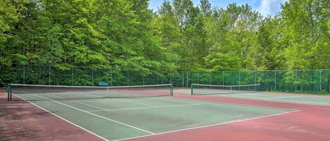 Cancha de tenis con red, rodeada de árboles.