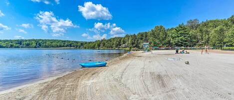 A beach with a boat, people, and a forested hill in the background.