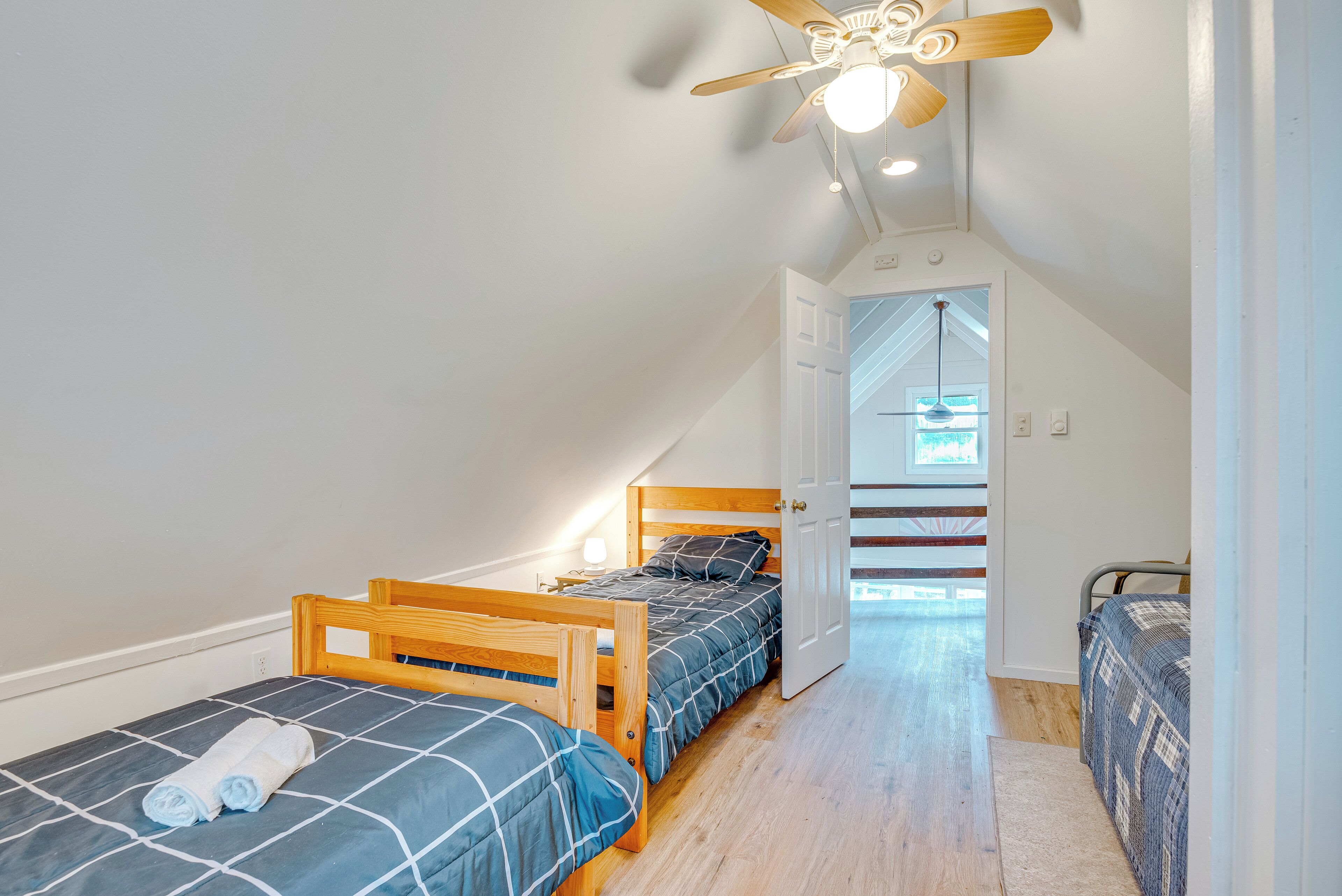 A bedroom with two wooden beds, a ceiling fan, and a door leading to a staircase.