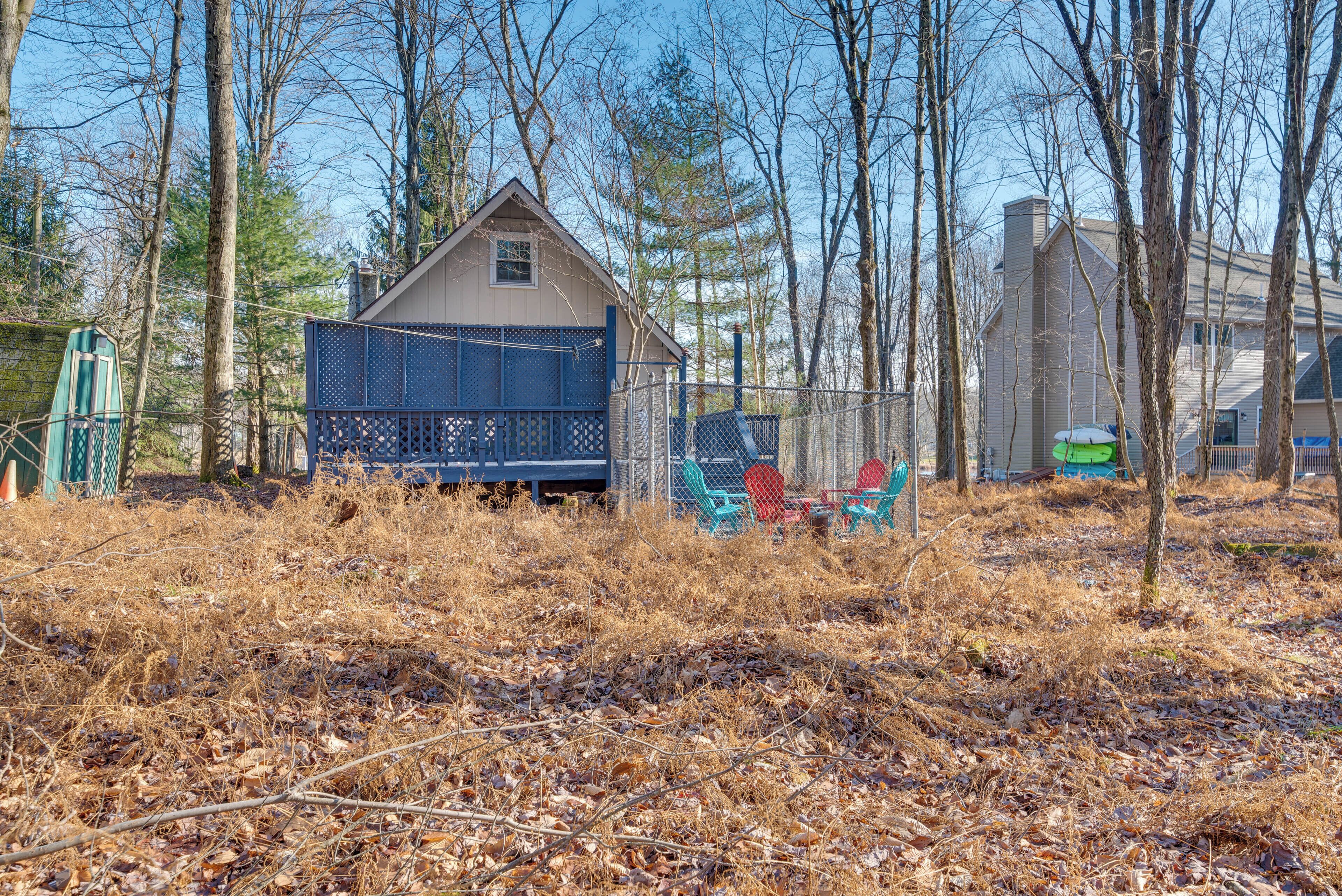 A small house with a fenced deck, surrounded by trees and dry grass.