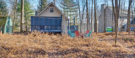 A small house with a fenced deck, surrounded by trees and dry grass.
