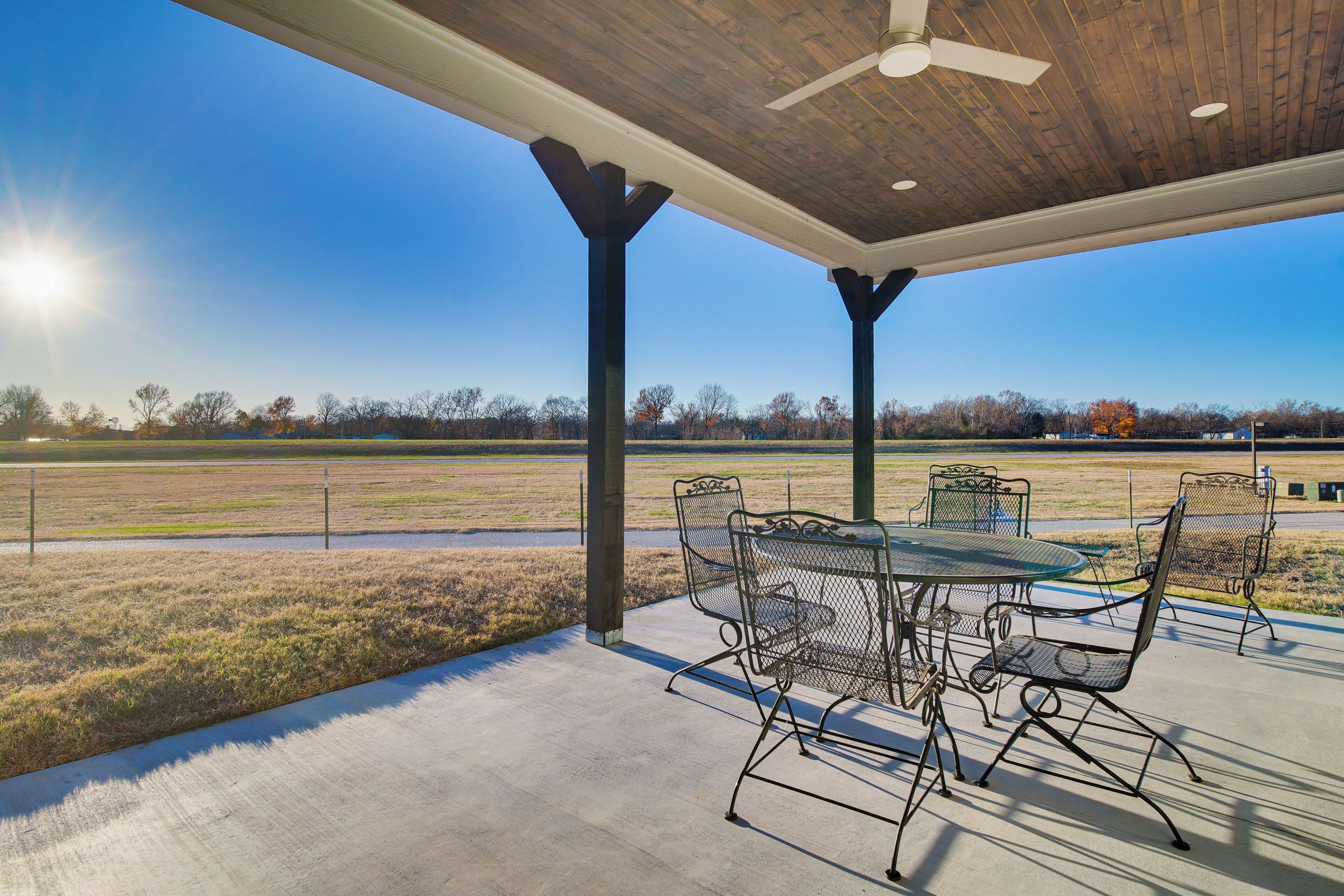 An outdoor patio with a table and chairs, a ceiling fan, and a view of a field and trees.