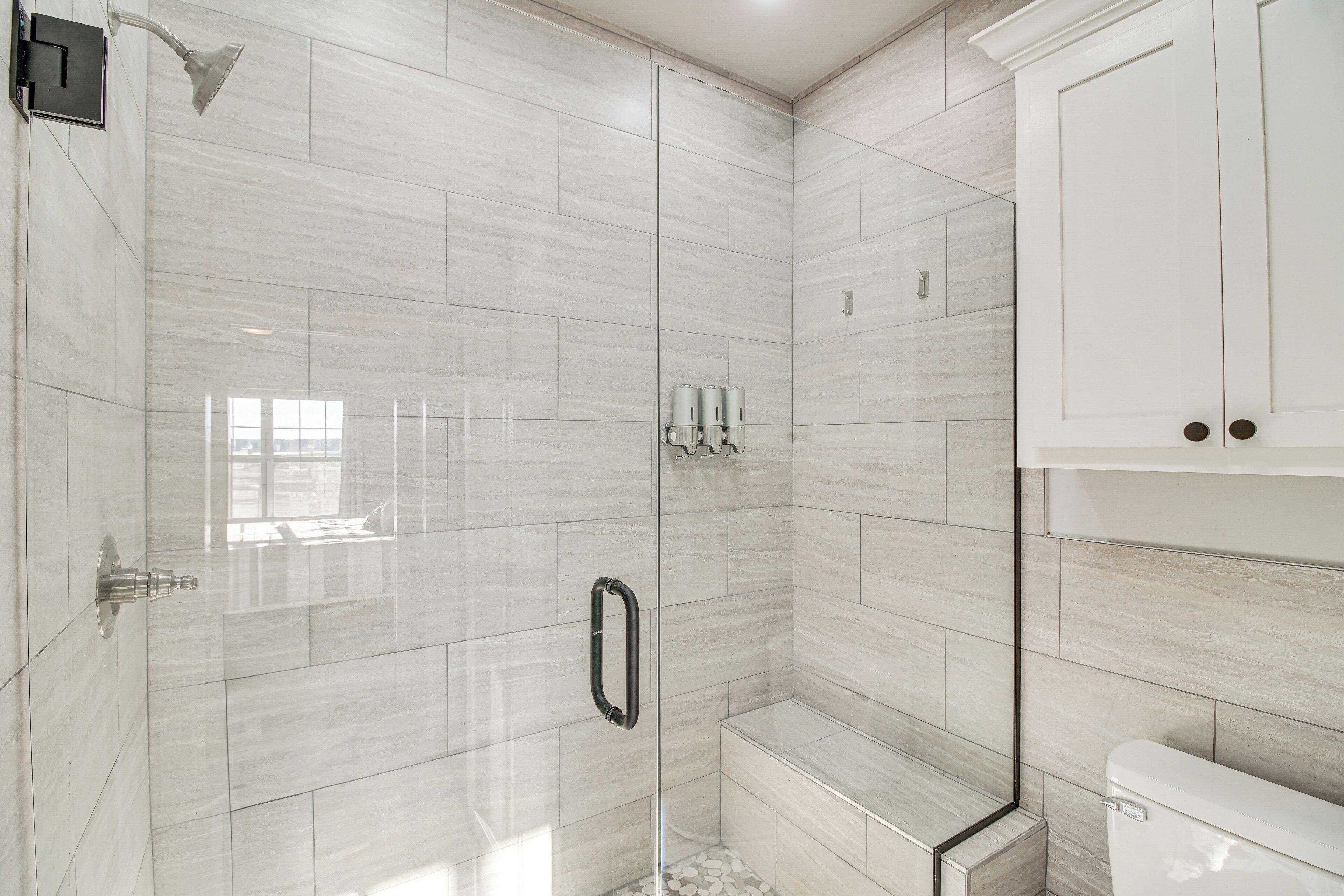 Une salle de bain moderne avec une douche à parois de verre, des murs recouverts de carreaux blancs et des toilettes.