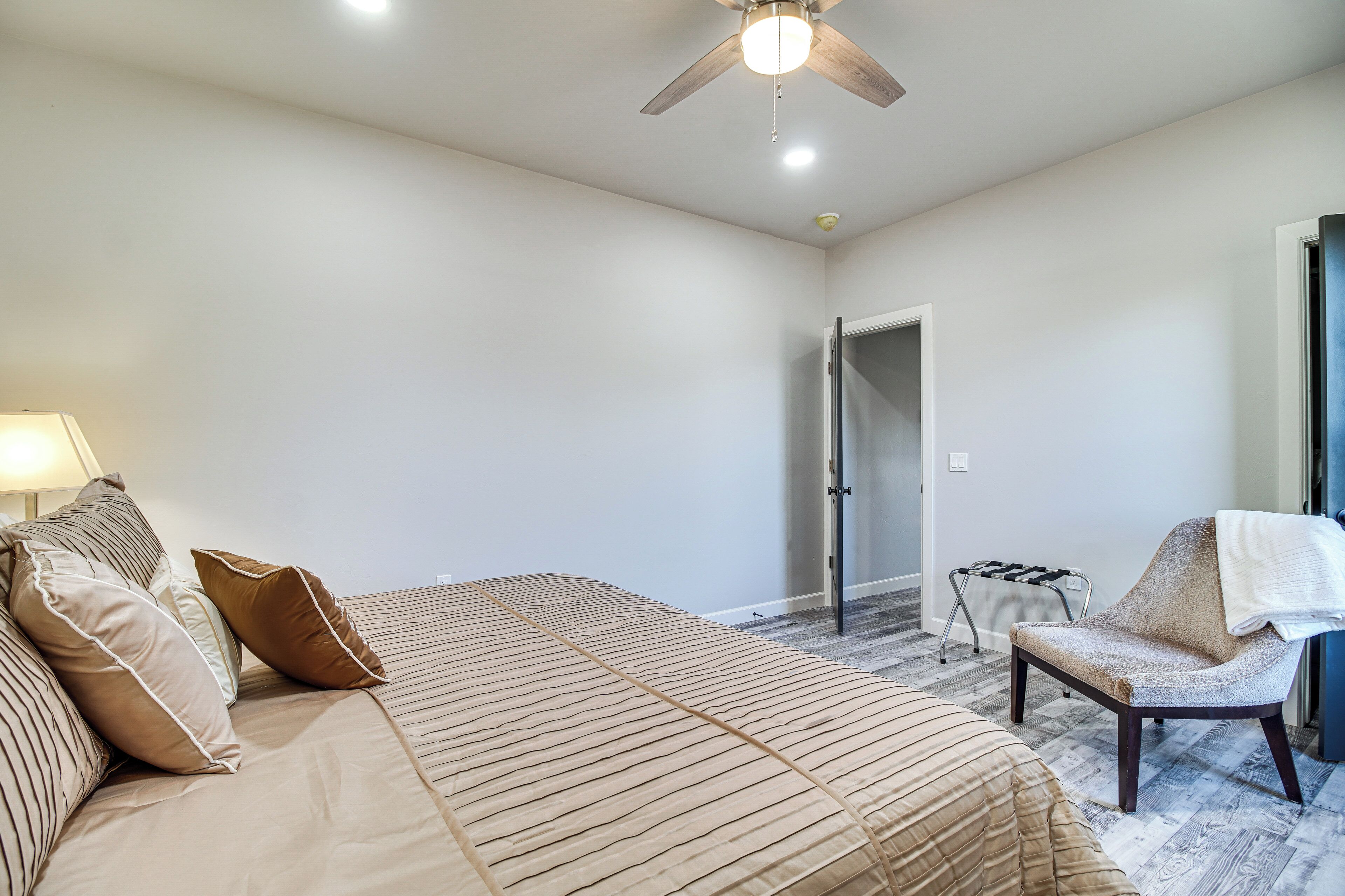 A bedroom with a bed, a chair, a ceiling fan, and a door.