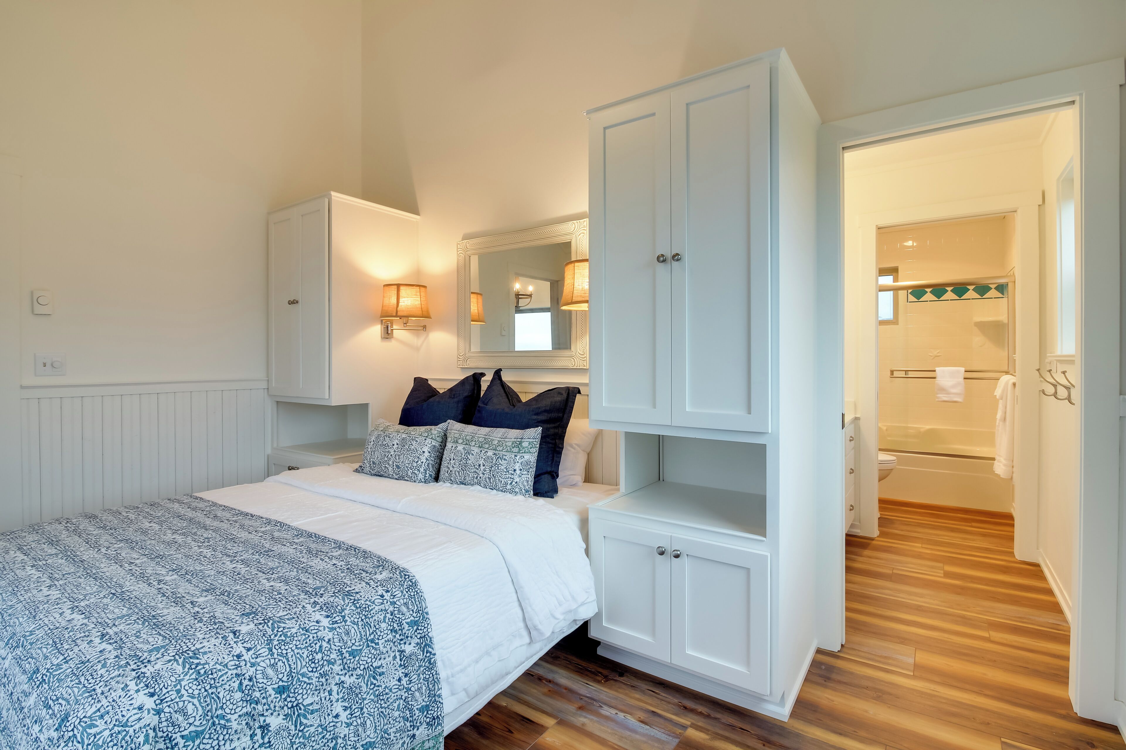 A bedroom with a bed, a wardrobe, a mirror, and a bathroom visible through an open door.