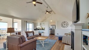 A spacious living room with a brown leather sofa, a wooden coffee table, and a blue rug. There are ceiling fans, a fireplace, and a bookshelf with books. - Scenic Bandon Vacation Rental w/ Beach Access! (Bandon)