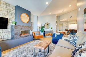 Una sala de estar moderna con chimenea de piedra, televisor de pantalla plana y un área de estar acogedora con sofá y reposapiés.