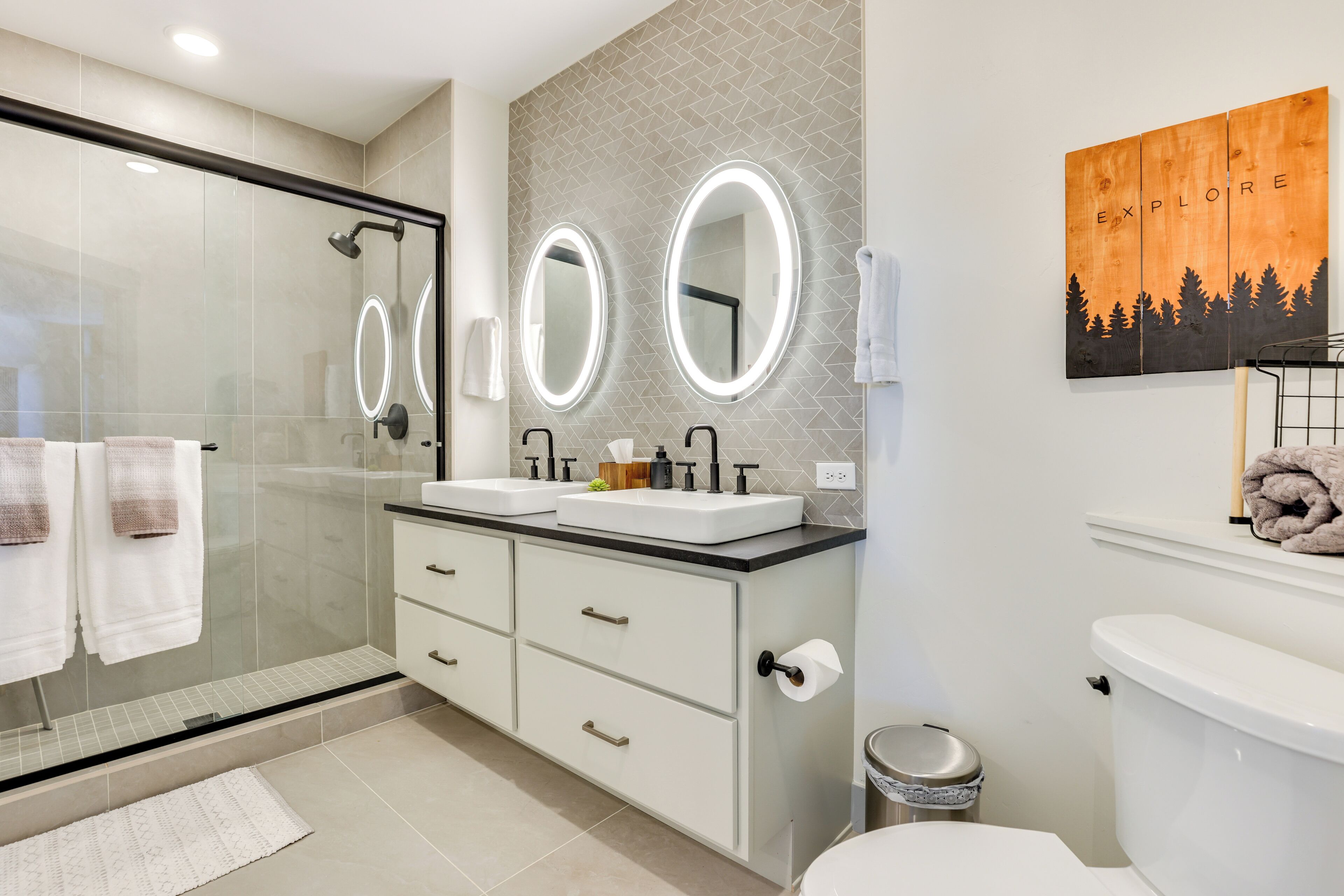 Une salle de bain moderne avec une douche à l’italienne en verre, deux vasques et des toilettes.
