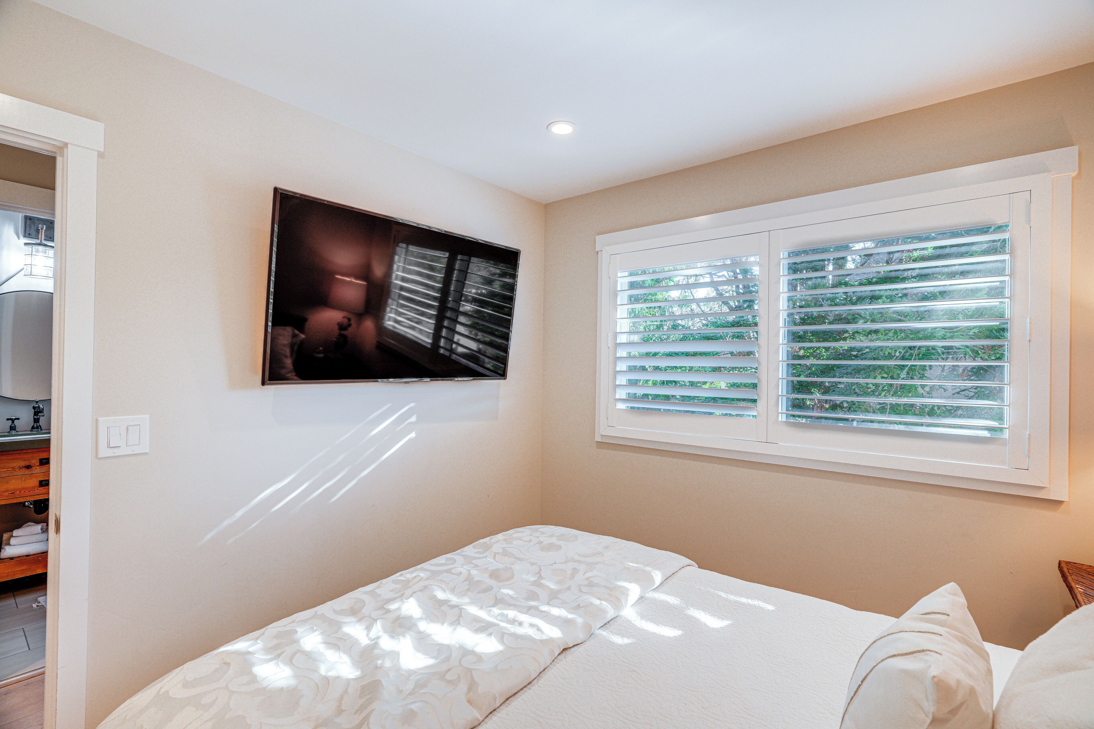 A bedroom with a bed, a TV mounted on the wall, and a window with blinds.