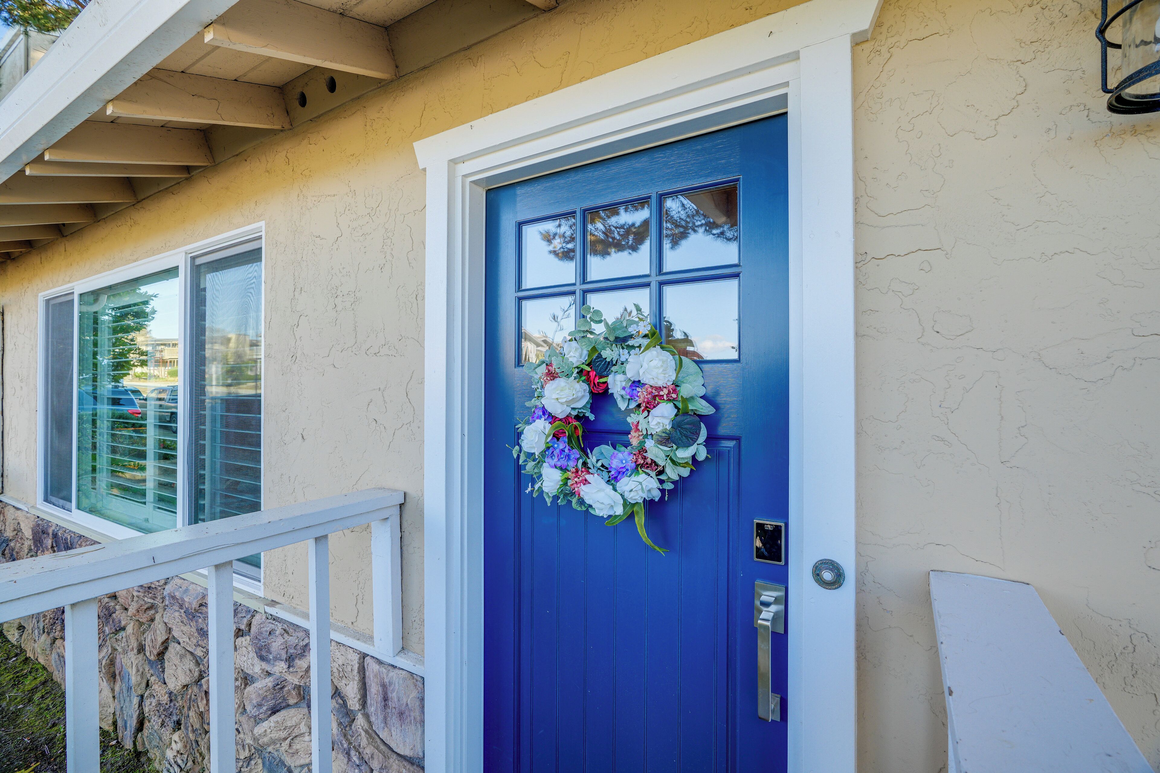 A blue door with a floral wreath, a stone wall, and a white railing.