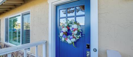 A blue door with a floral wreath, a stone wall, and a white railing.