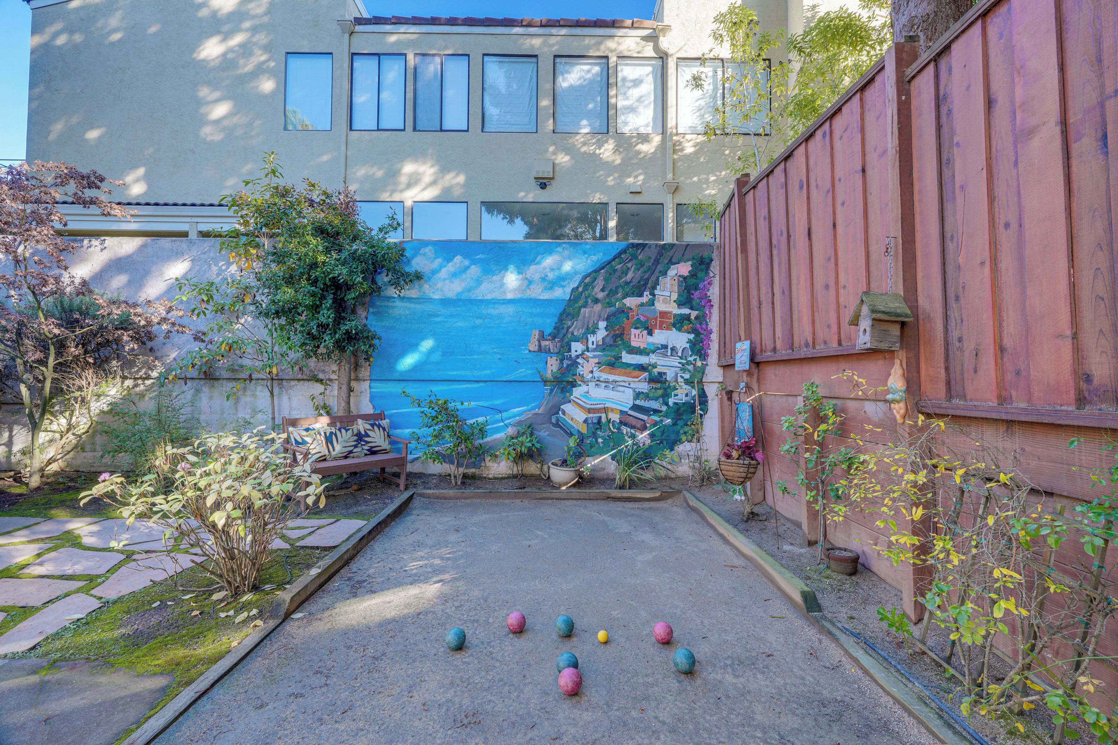 Un patio con un mural colorido, una zona de estar y una cancha de bochas.