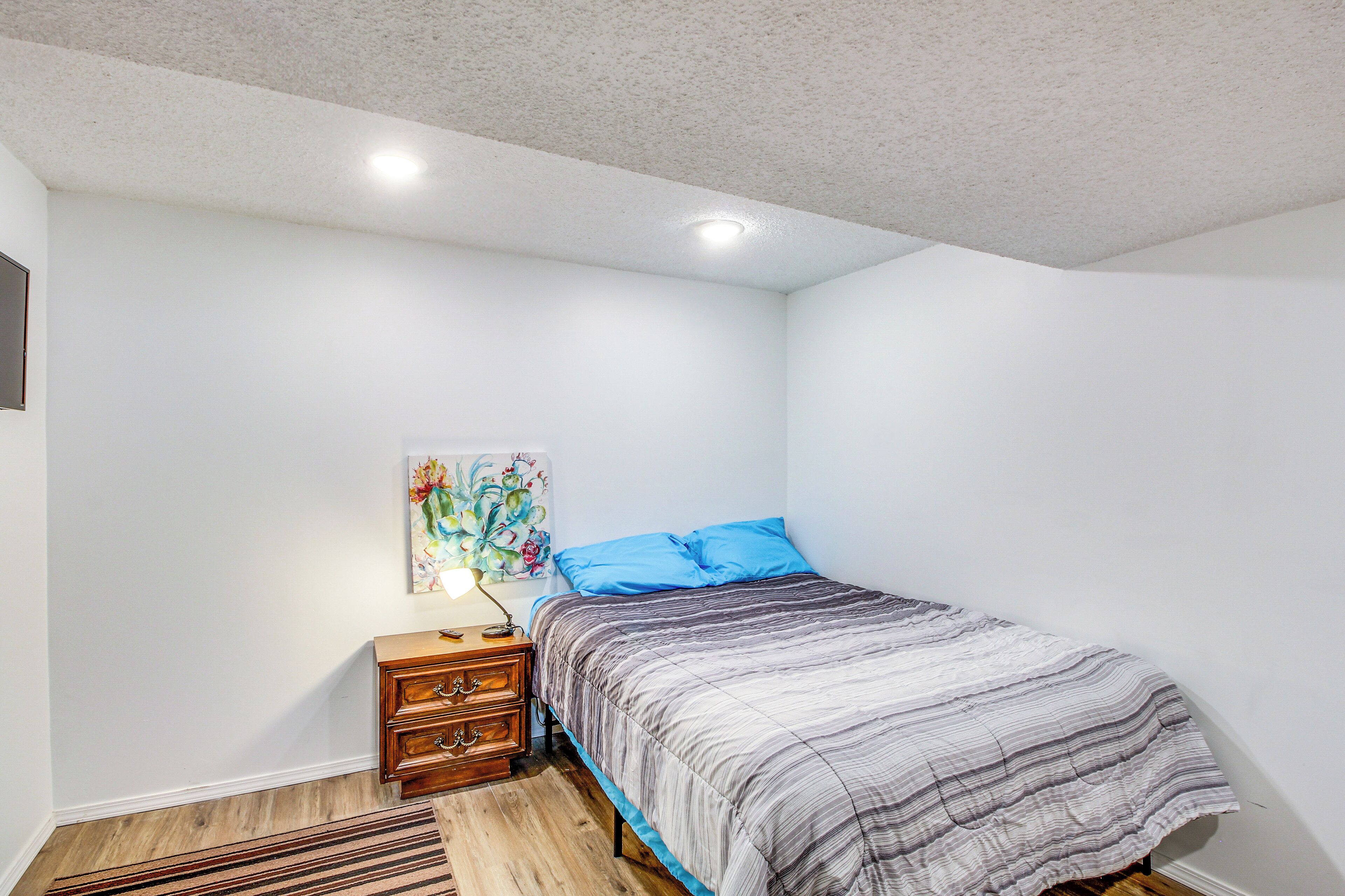 A bedroom with a bed, a nightstand, a lamp, and a painting on the wall.