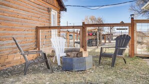 Hirsimökki, jossa on kaksi Adirondack-tyylistä puutarhatuolia, nuotiopaikka ja puinen pergola.