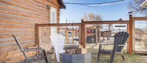 A log cabin with two Adirondack chairs, a fire pit, and a wooden pergola.