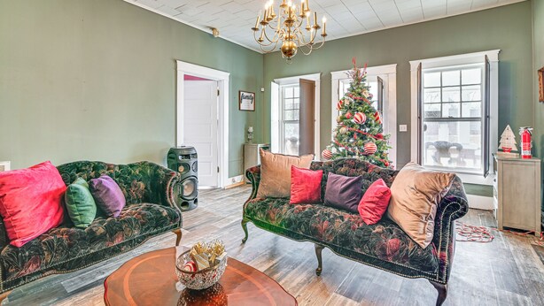 A living room with two green upholstered sofas with colorful cushions, a chandelier, a Christmas tree, and a large window with a view of the outside. - Historic Aberdeen Vacation Home w/ Yard! (Aberdeen)