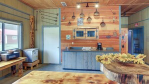 A rustic kitchen with wooden walls, a central island, and various kitchen utensils hanging on the wall. - Montana Cabin: Day Trip to Glacier Natl Park! (De Borgia)