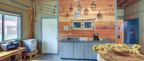 A rustic kitchen with wooden walls, a central island, and various kitchen utensils hanging on the wall.