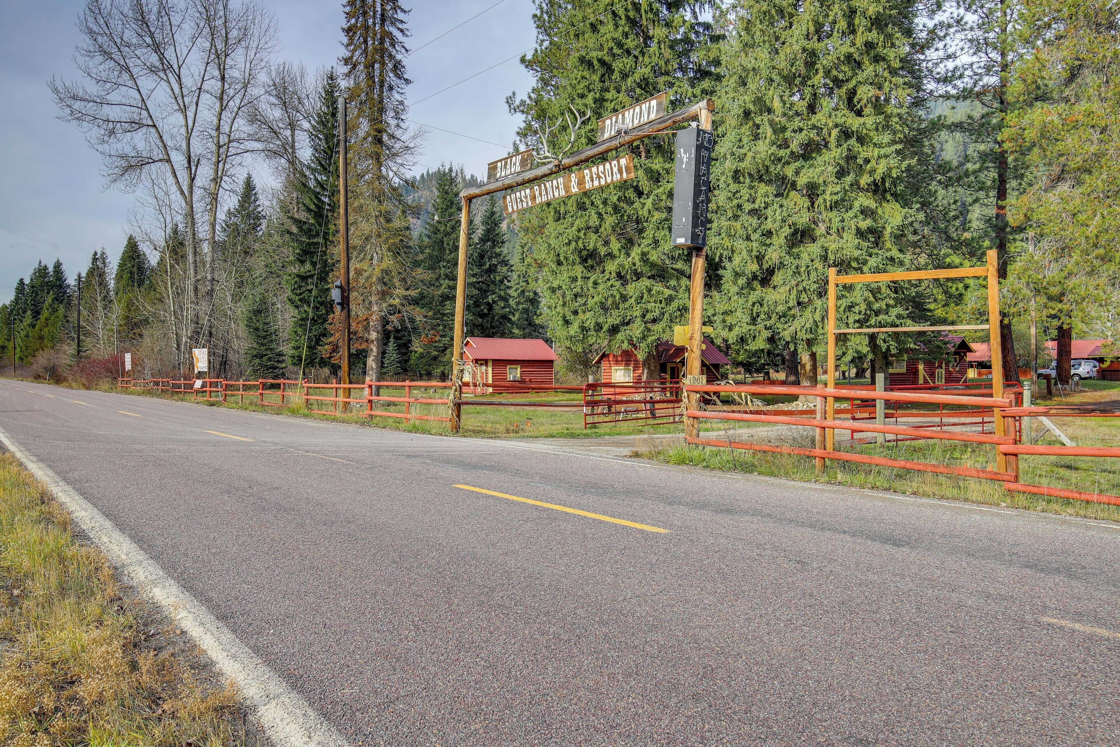 A wooden signpost with 'Diamond Guest Ranch & Resort' written on it, surrounded by a red fence and trees.