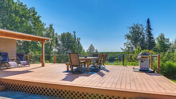 Een houten terras met tuinmeubilair, een barbecue en uitzicht op bomen en een meer.