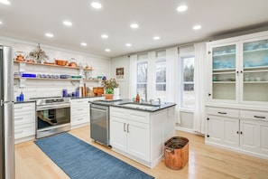 A modern kitchen with white cabinetry, stainless steel appliances, and a large window with curtains.