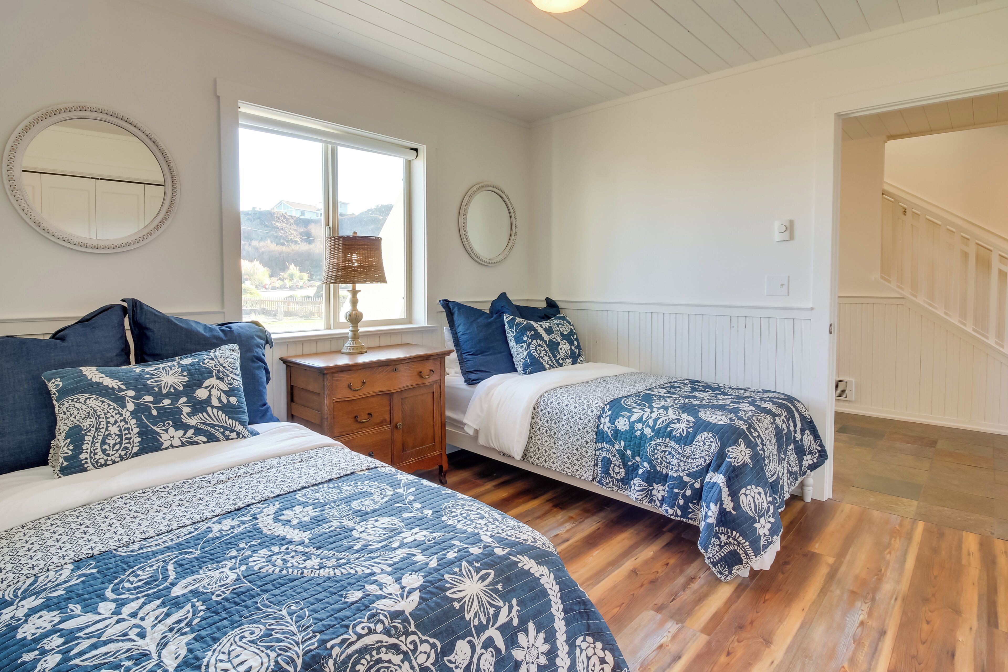 A bedroom with two beds, wooden flooring, and a window with a view.