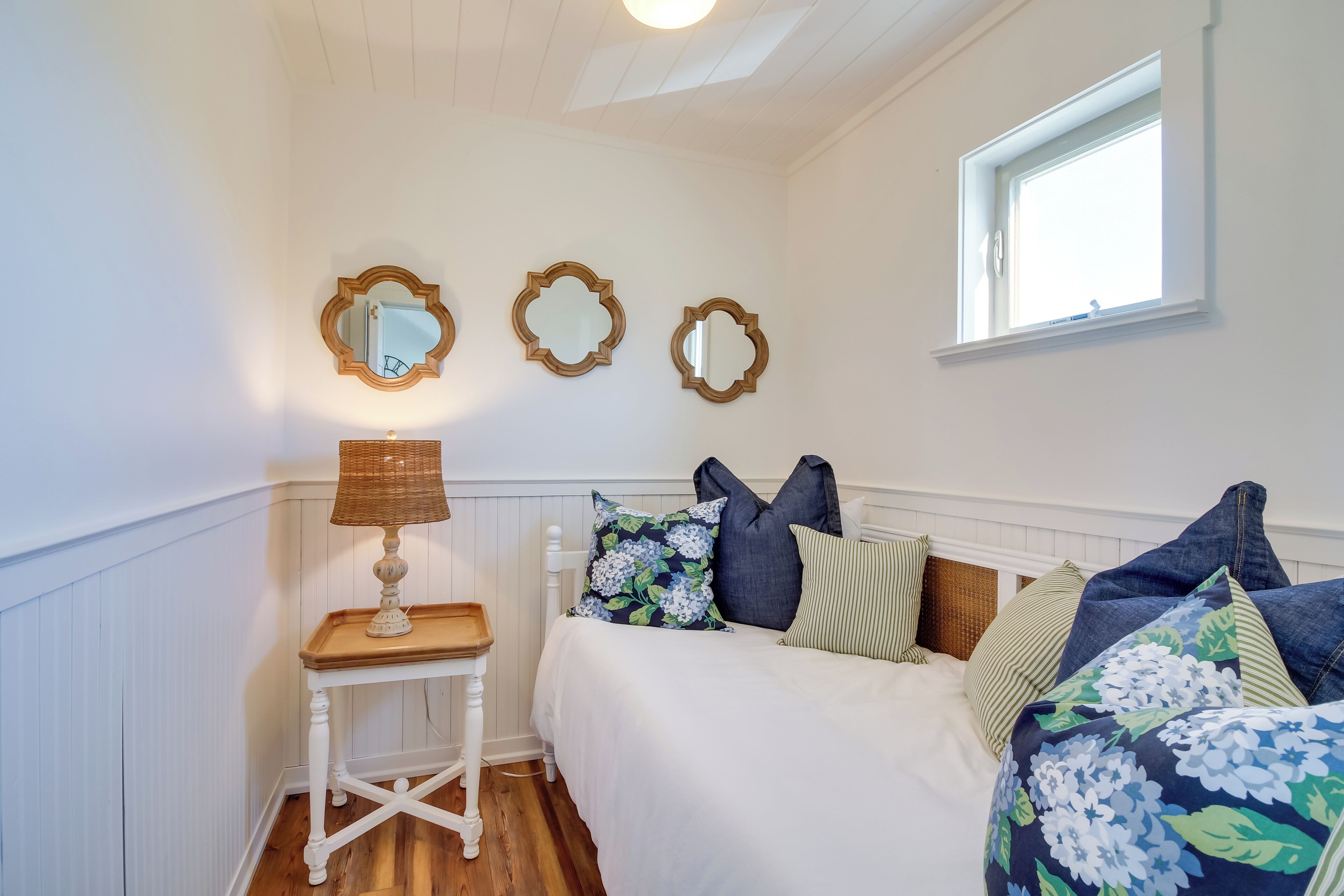 A bedroom with a bed, a nightstand, a lamp, and three wall-mounted mirrors.