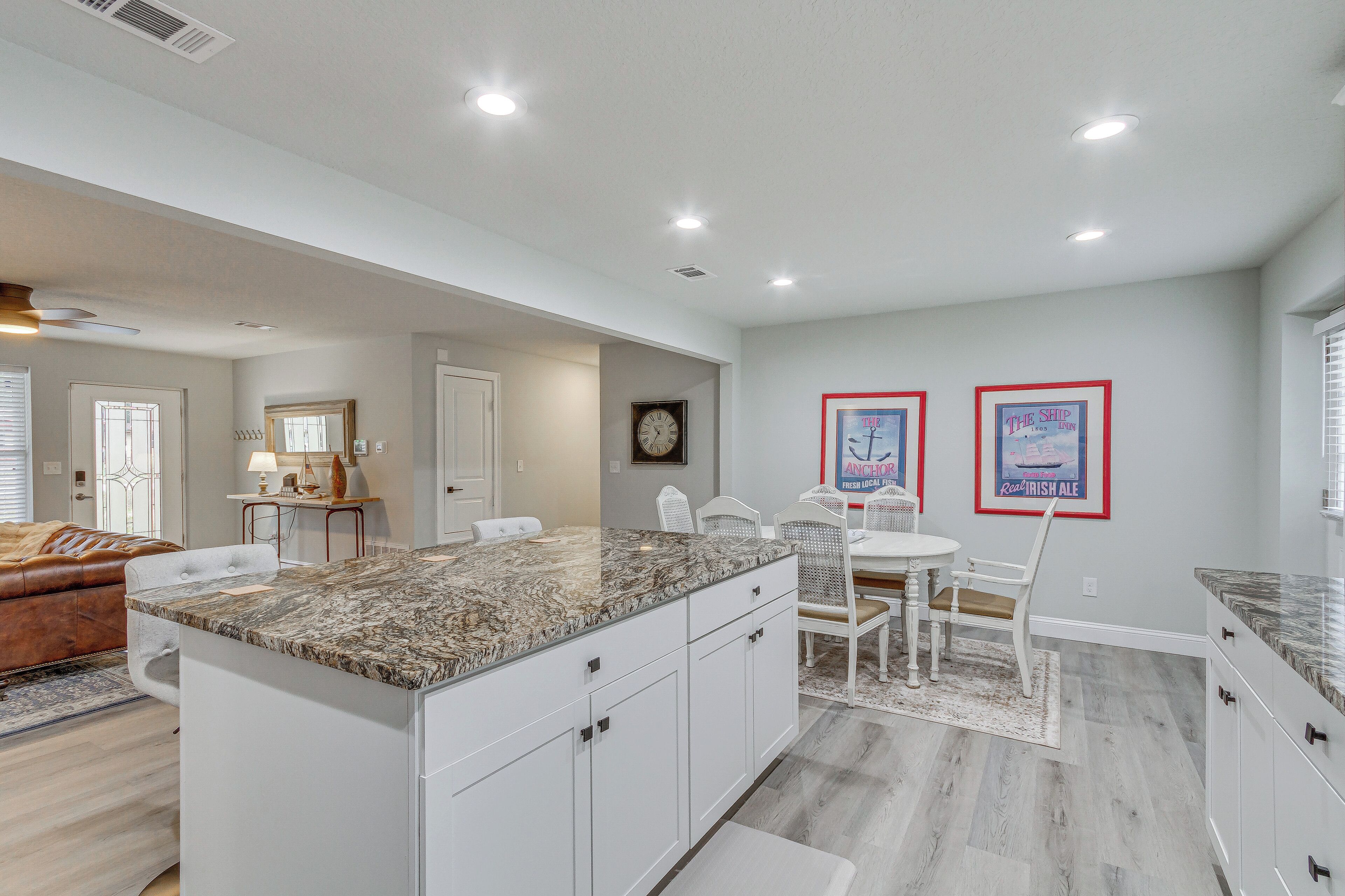 A modern kitchen with white cabinets, granite countertops, and a dining area with white chairs.