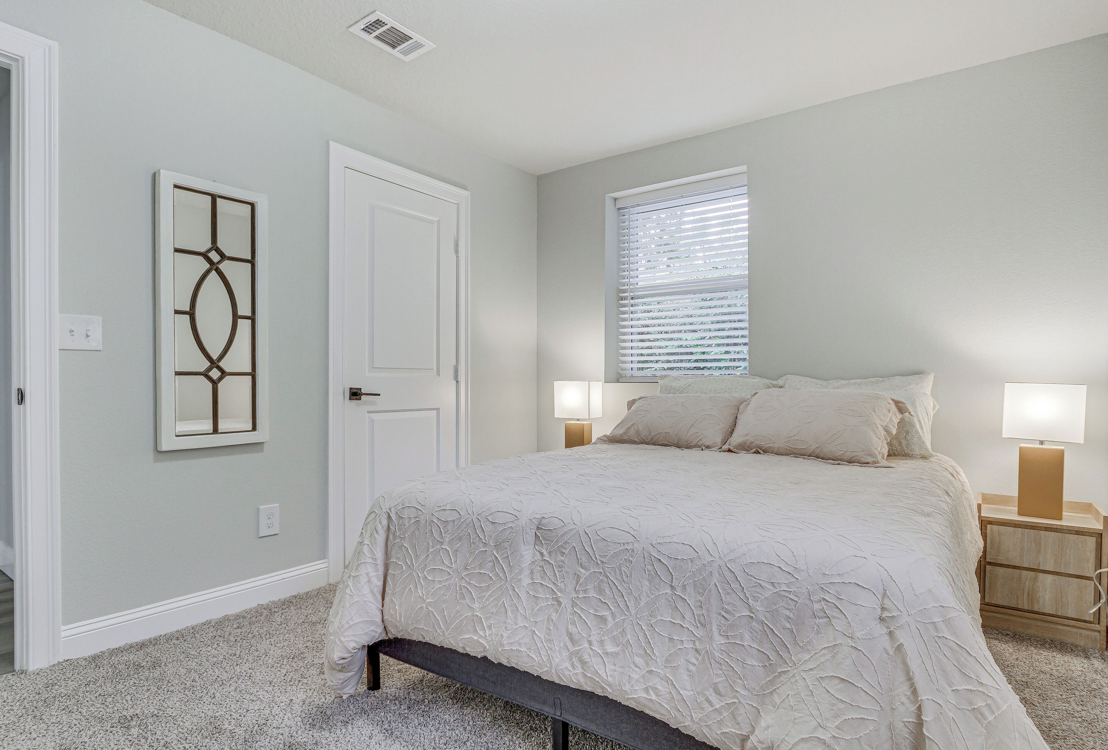 A bedroom with a bed, bedside lamps, a window with blinds, and a door.