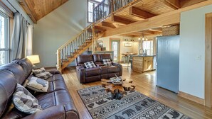 A spacious living area with a leather sofa, a wooden coffee table, and a patterned rug. A staircase leads to an upper level.