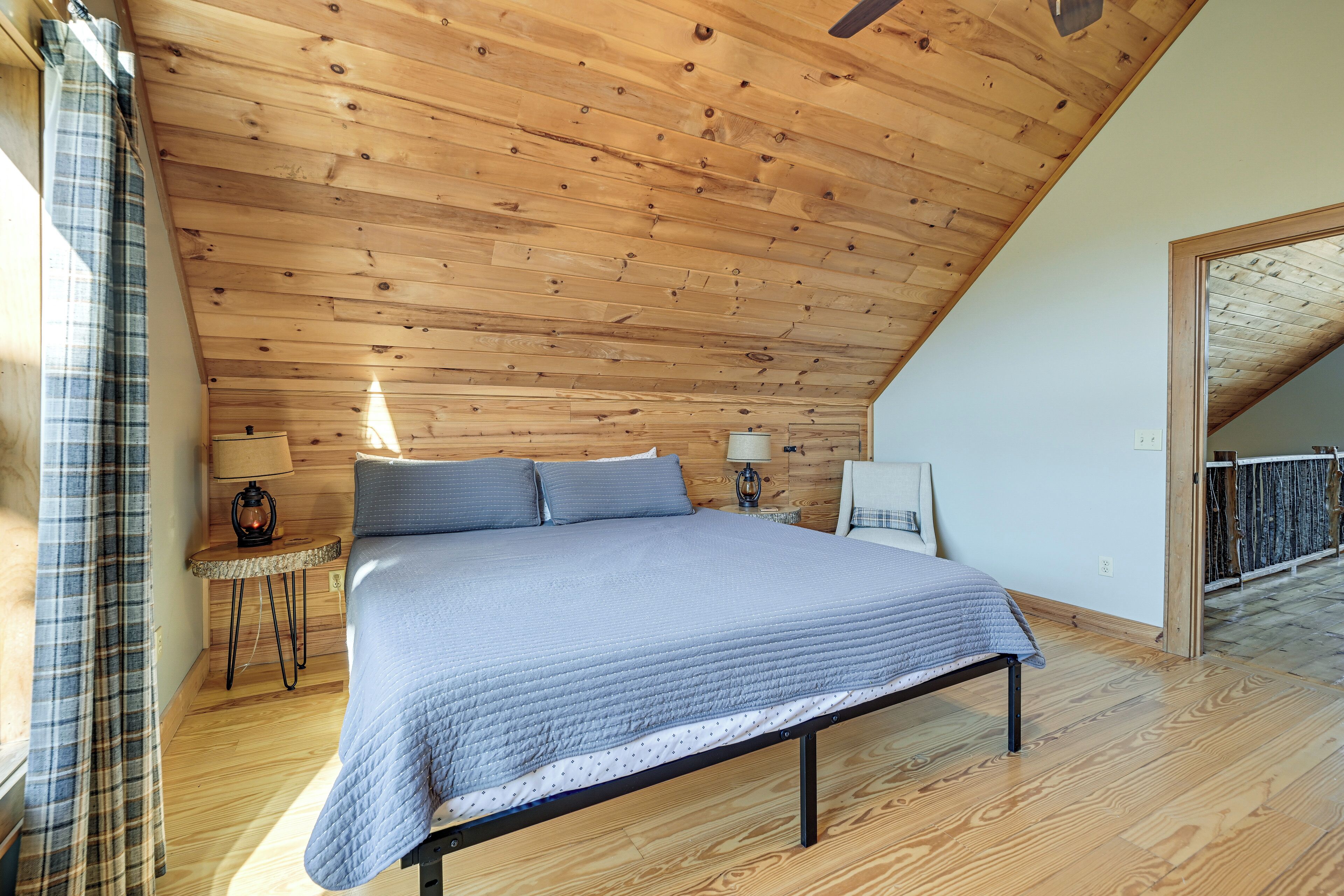 A bedroom with a wooden ceiling, a bed, a nightstand, a lamp, and a window with curtains.