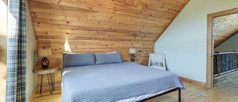A bedroom with a wooden ceiling, a bed, a nightstand, a lamp, and a window with curtains.